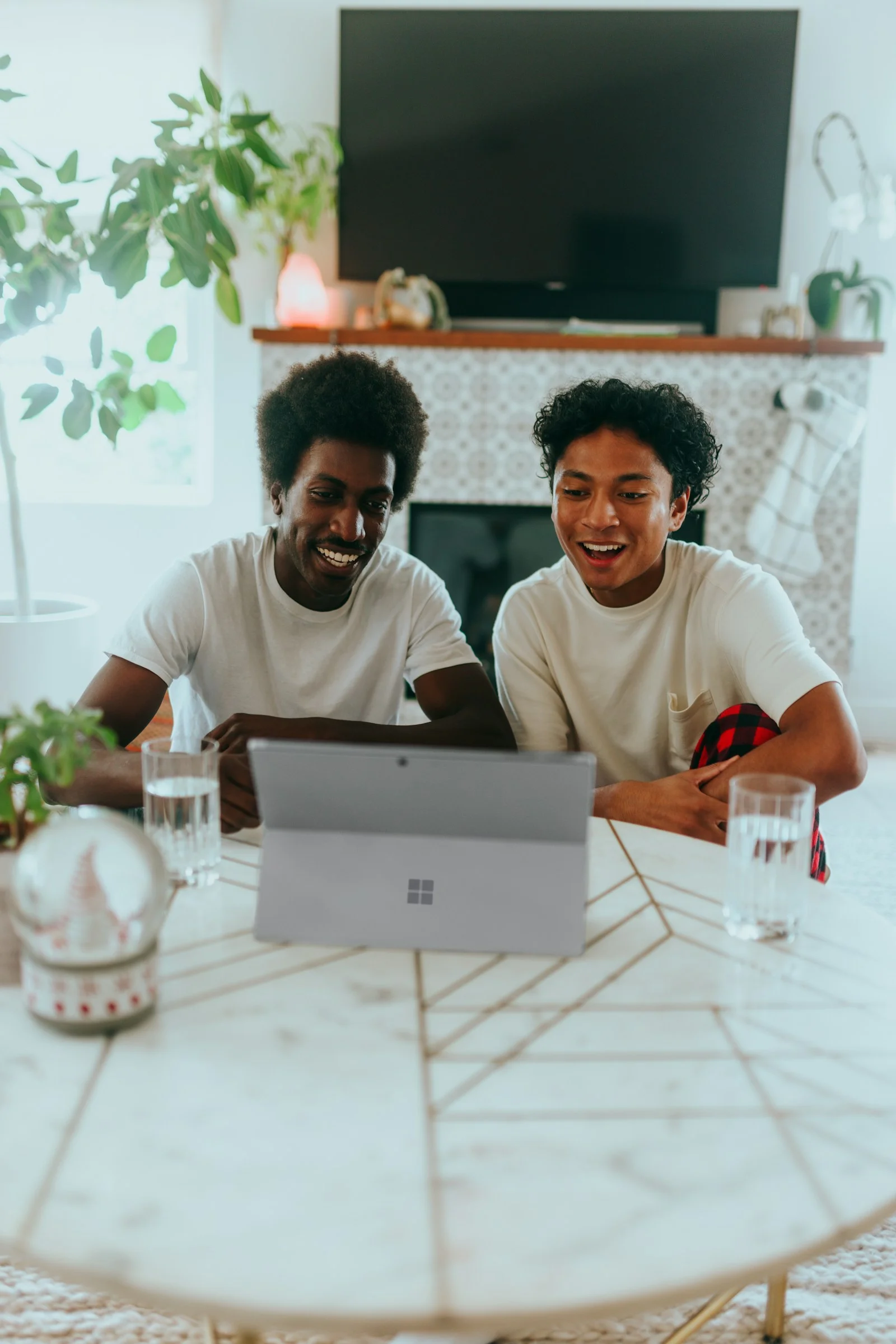 Duas pessoas sorrindo enquanto usam um computador à mesa de casa.
